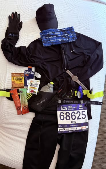 Race morning flat lay for the 2025 NYC Marathon: black running kit, cap, gloves, gels, a Garmin watch, and bib 68625