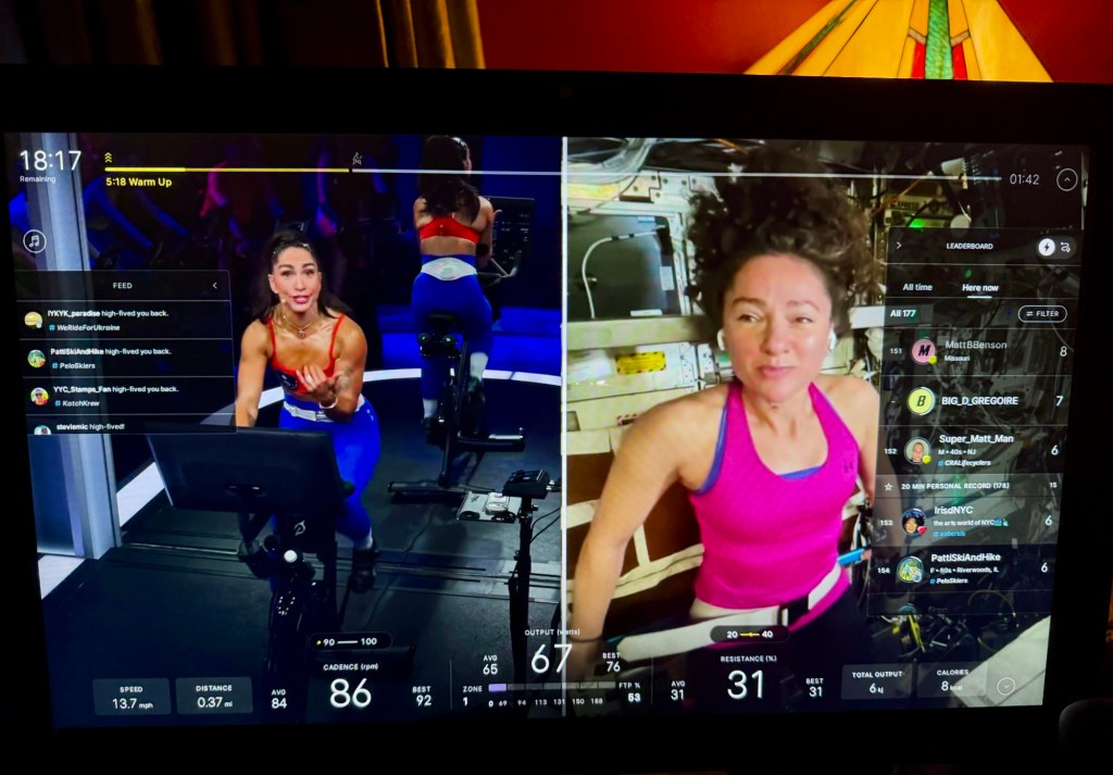 Peloton screen showing Robin Arzón riding in the studio beside astronaut Dr. Jessica Meir aboard the International Space Station, with the class leaderboard