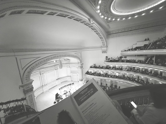 View from the upper balcony of Carnegie Hall looking down at the stage, with a concert program in the foreground