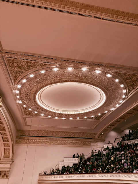 The ornate oval ceiling of Carnegie Hall's Stern Auditorium, ringed with lights, above the balconies